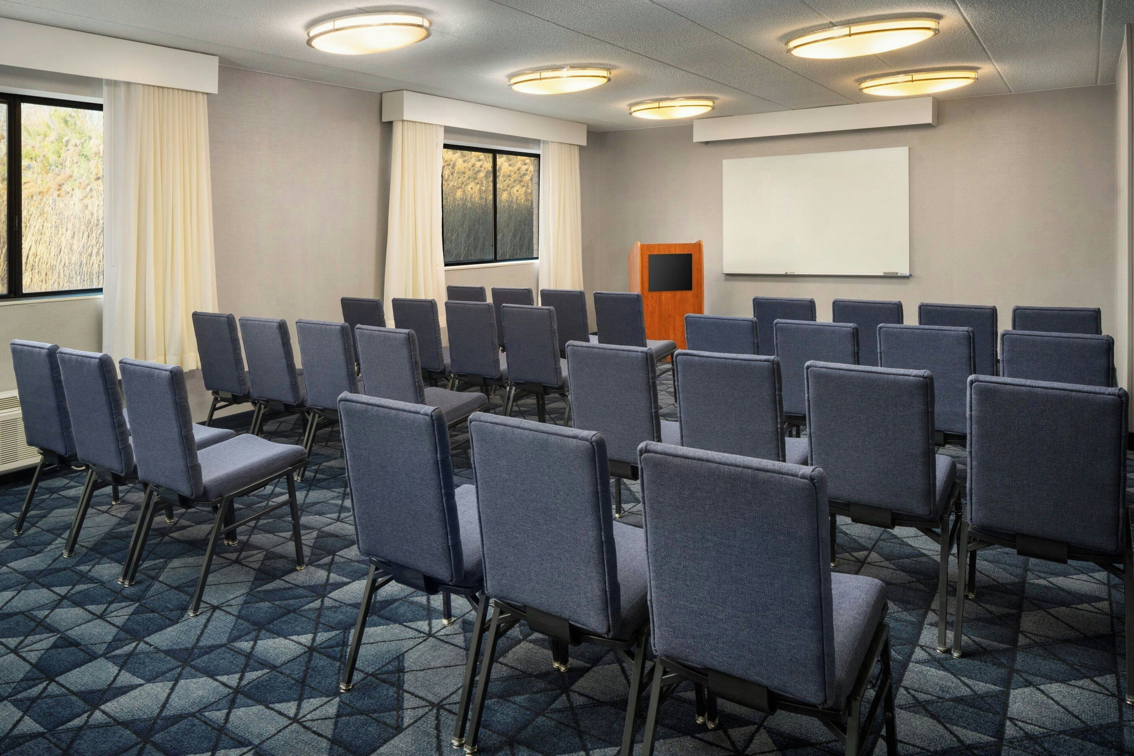Een congreszaal met rijen stoelen, een projectiescherm en een spreekgestoelte.