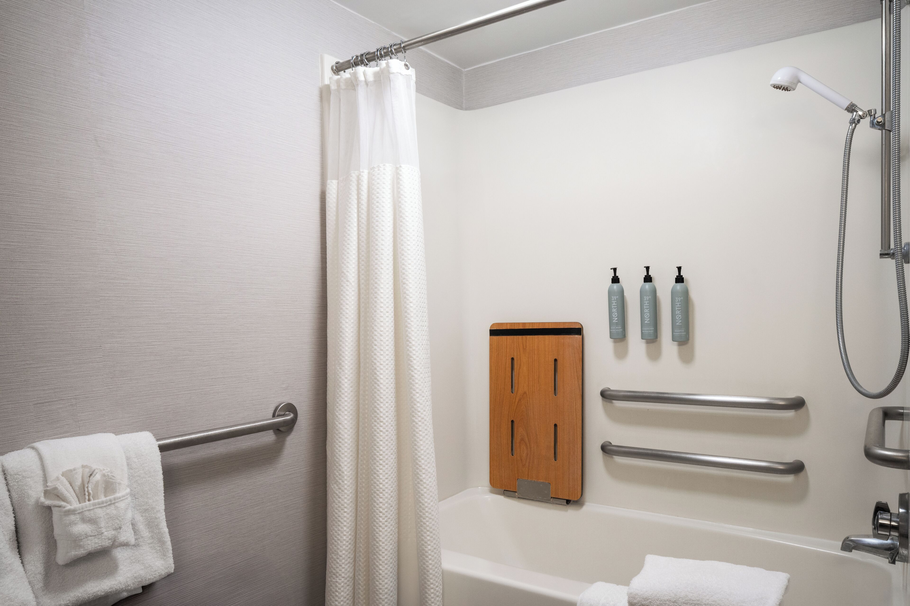 A bathroom with a bathtub, a shower, a towel rack, and a wooden panel with hand sanitizer bottles.