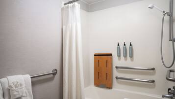 A bathroom with a bathtub, a shower, a towel rack, and a wooden panel with hand sanitizer bottles.