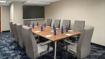 A conference room with a large table, eight chairs, a projector screen, and water bottles on the table.