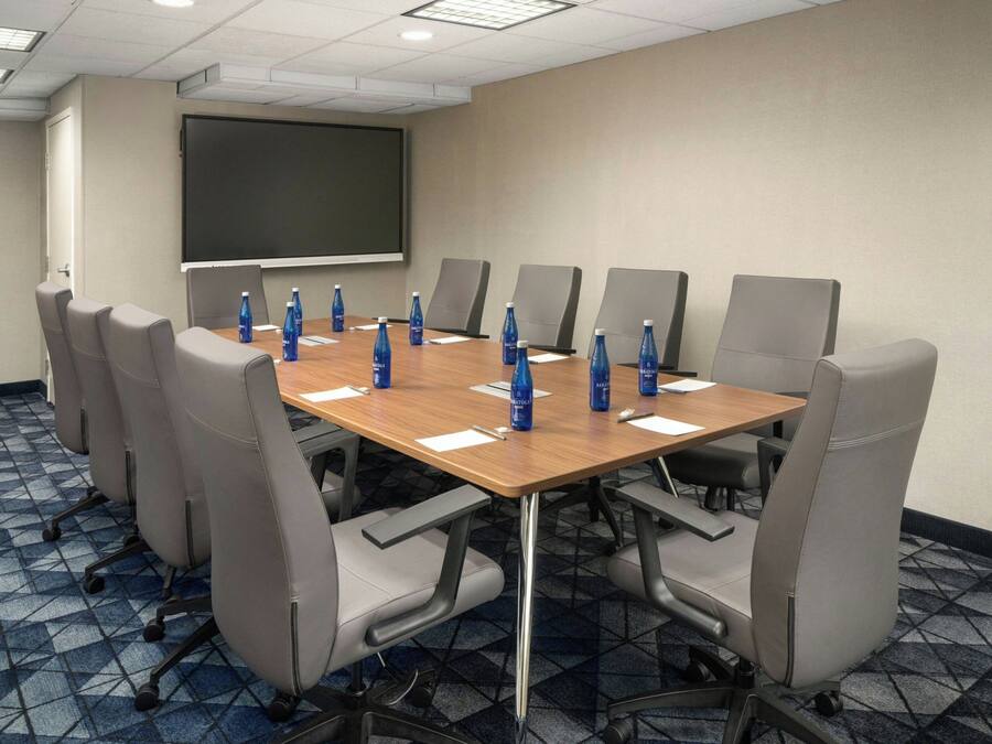 A conference room with a large table, eight chairs, a projector screen, and water bottles on the table.