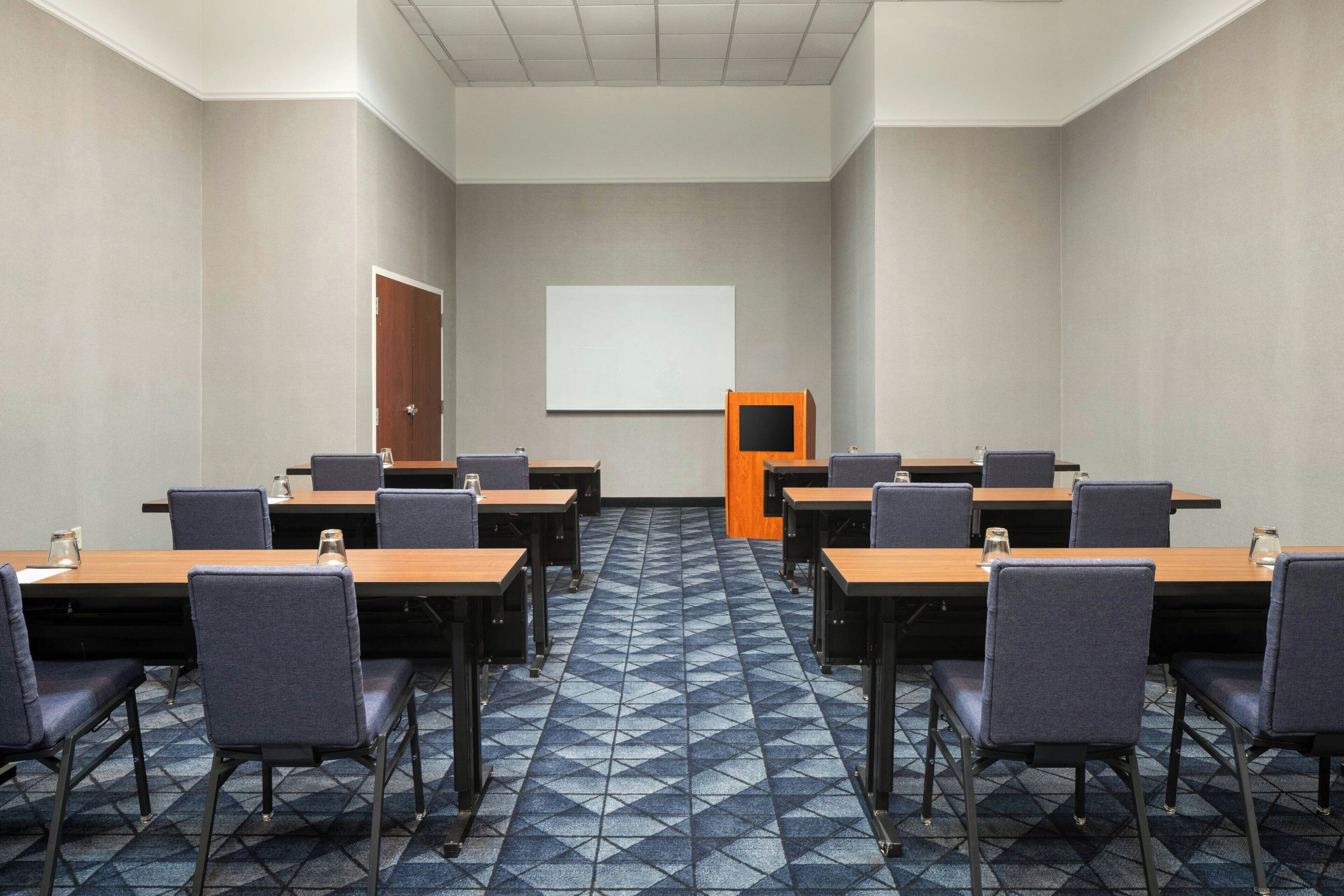 Une salle de conférence équipée de tables et de chaises, d’un tableau blanc et d’une porte.