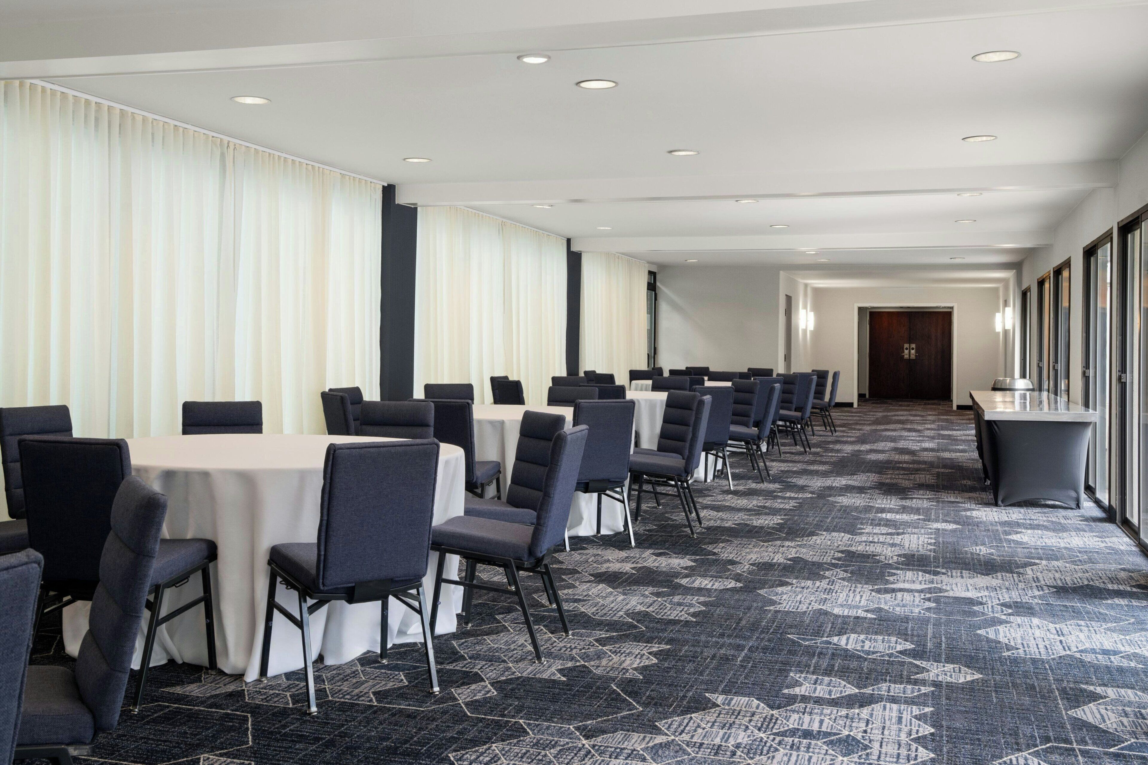 A conference room with rows of tables and chairs, a patterned carpet, and a long corridor with doors.