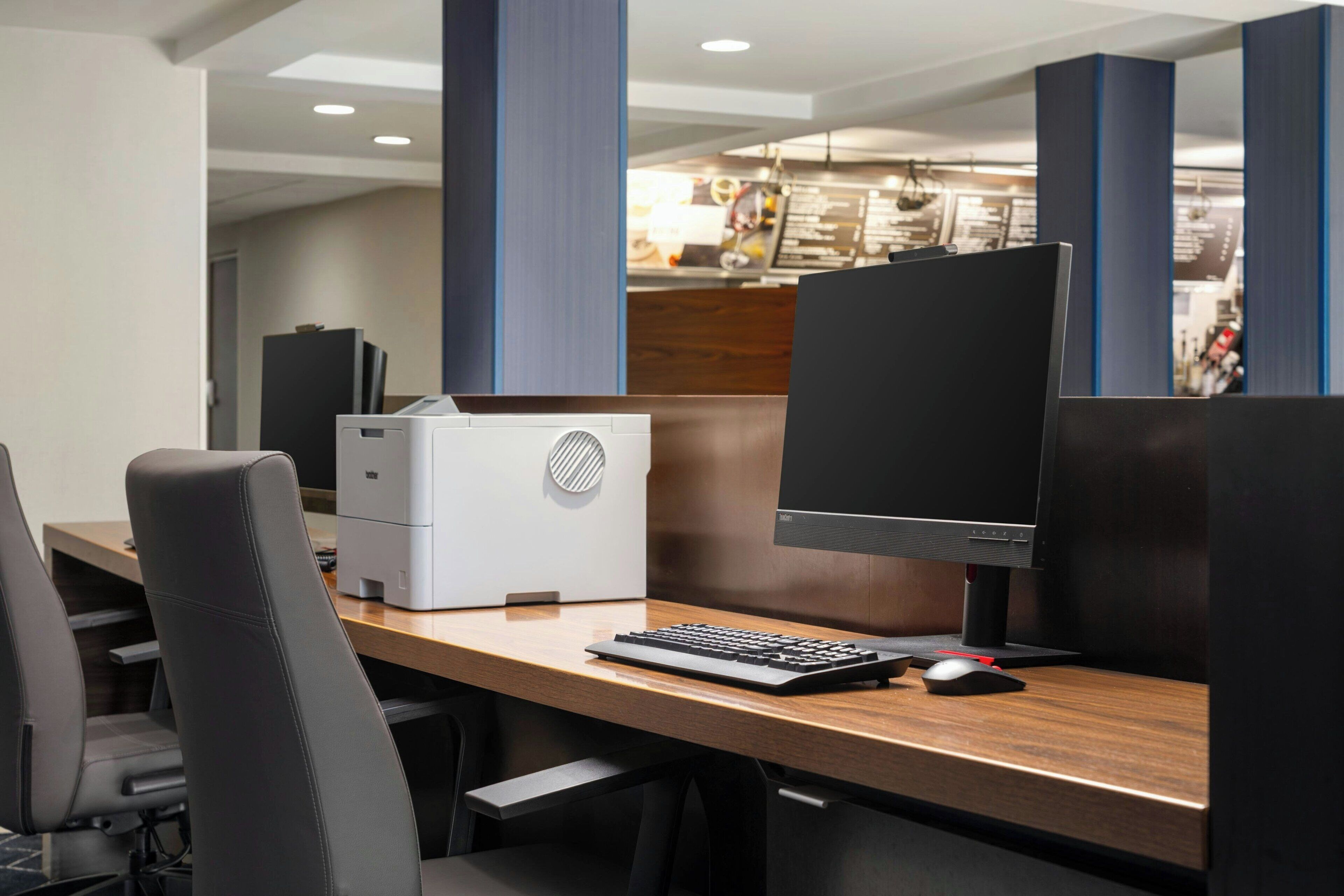 Un espacio de oficina moderno con un escritorio de madera, una computadora de escritorio, una impresora y un monitor grande.