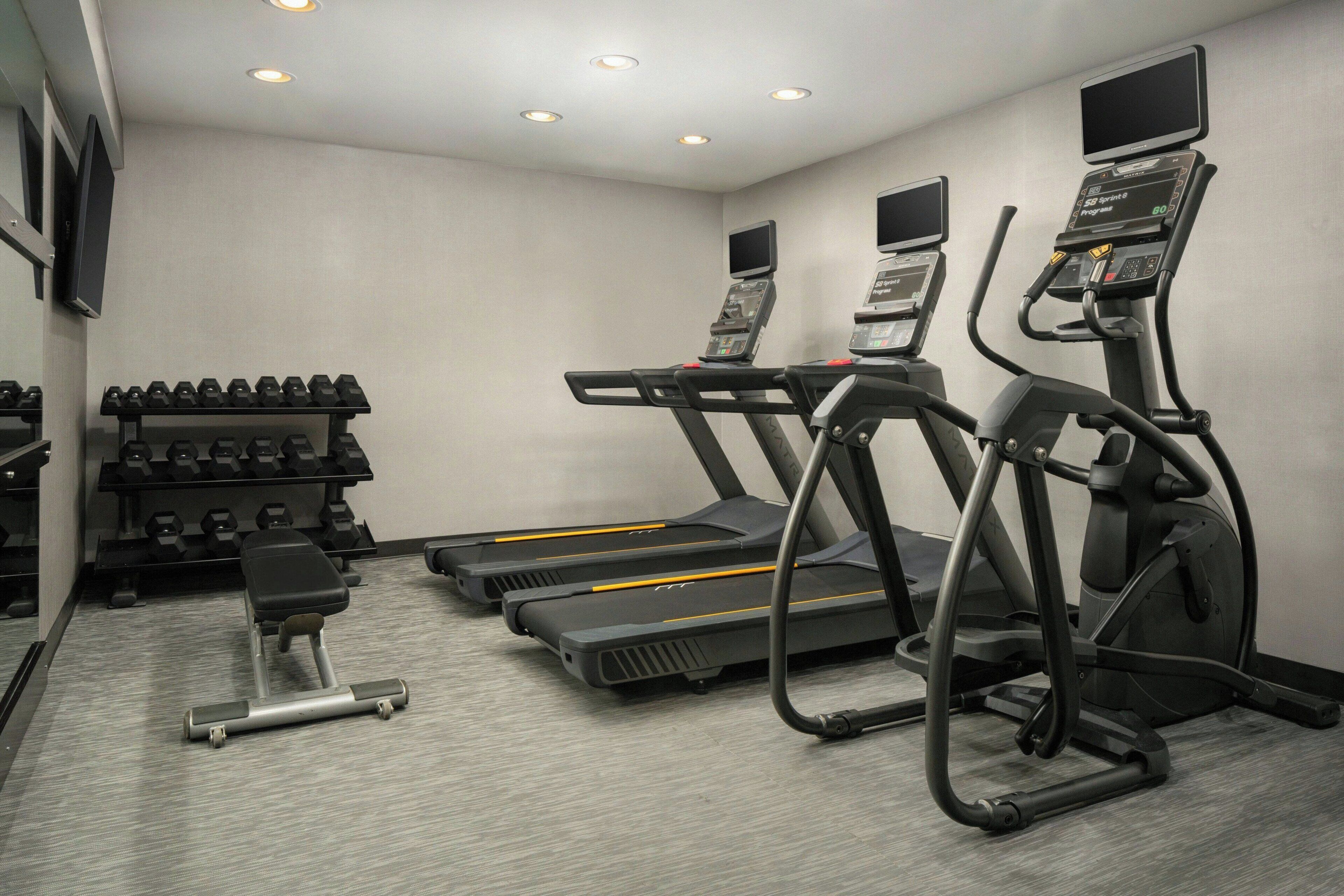 A gym with treadmills, dumbbells, and a bench.