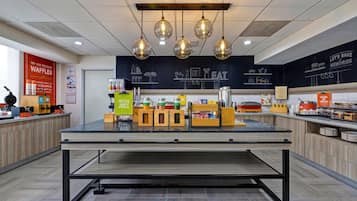 Un área de cocina moderna con una isla central, luces colgantes y una pared de pizarra con dibujos relacionados con la cocina.