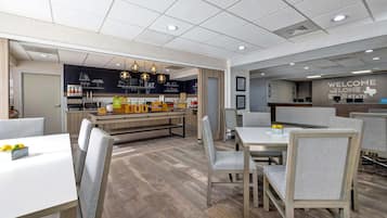 A modern dining area with a bar, seating arrangements, and a welcome sign.