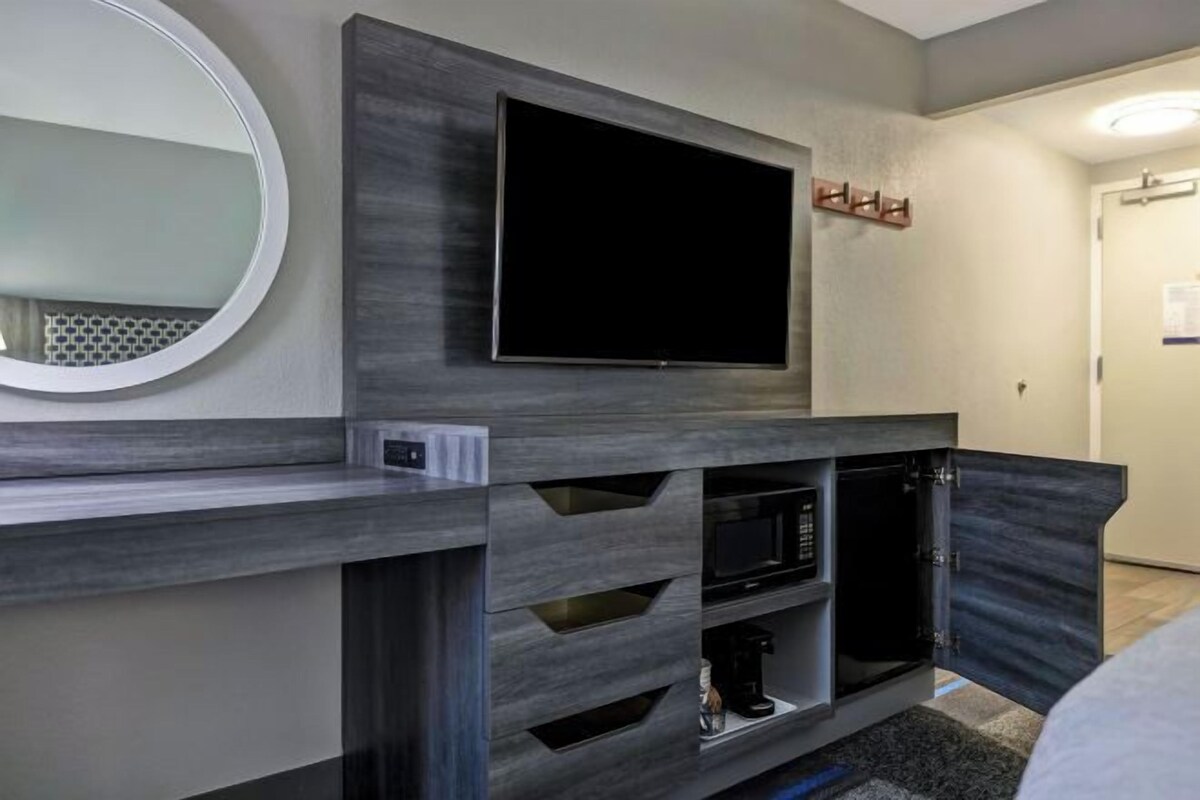 A modern living room with a flat-screen TV mounted on a wall, built-in entertainment unit with a coffee maker, and a round mirror on the left.