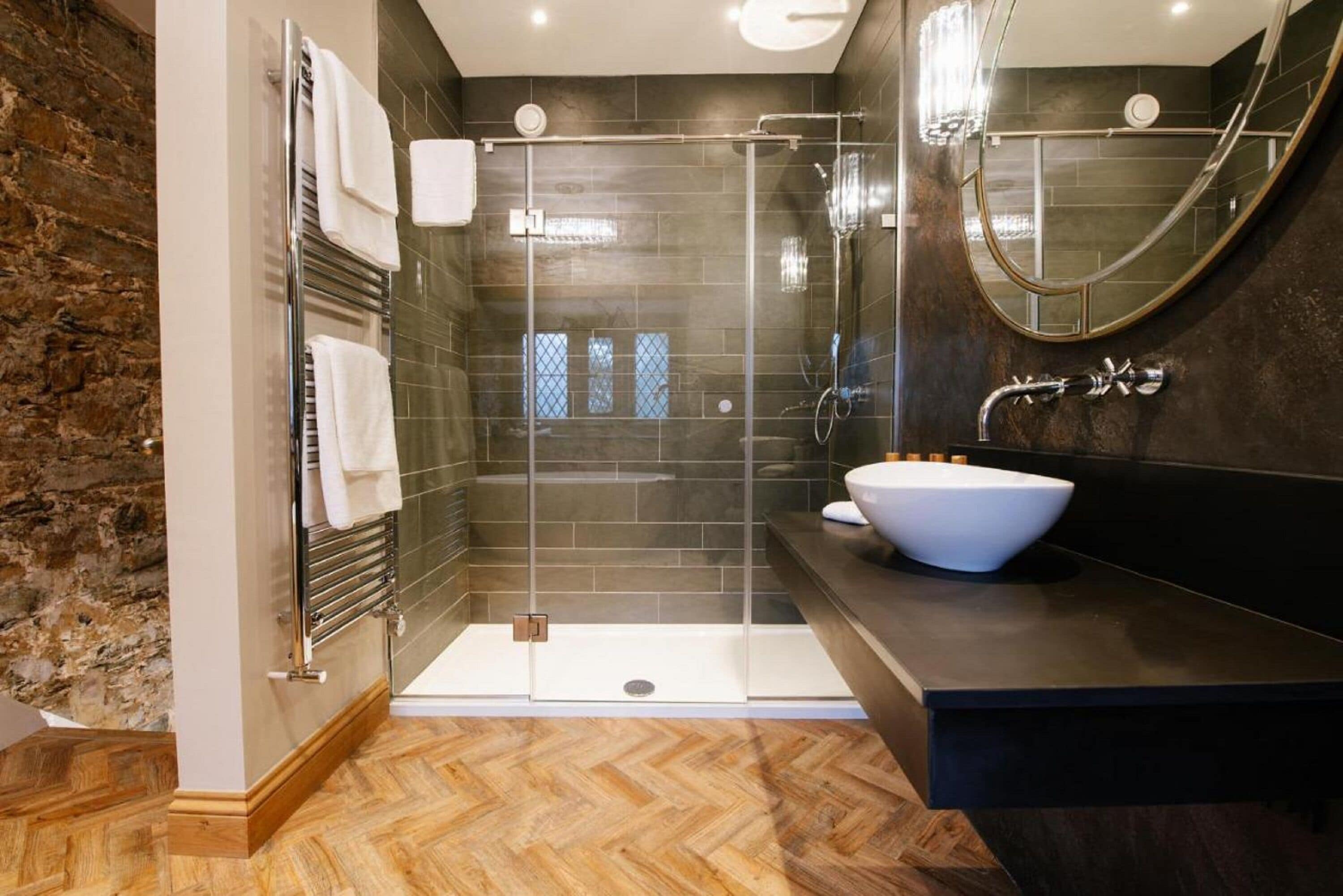 Un baño moderno con ducha de vidrio, un lavamanos blanco tipo pedestal y un espejo grande.