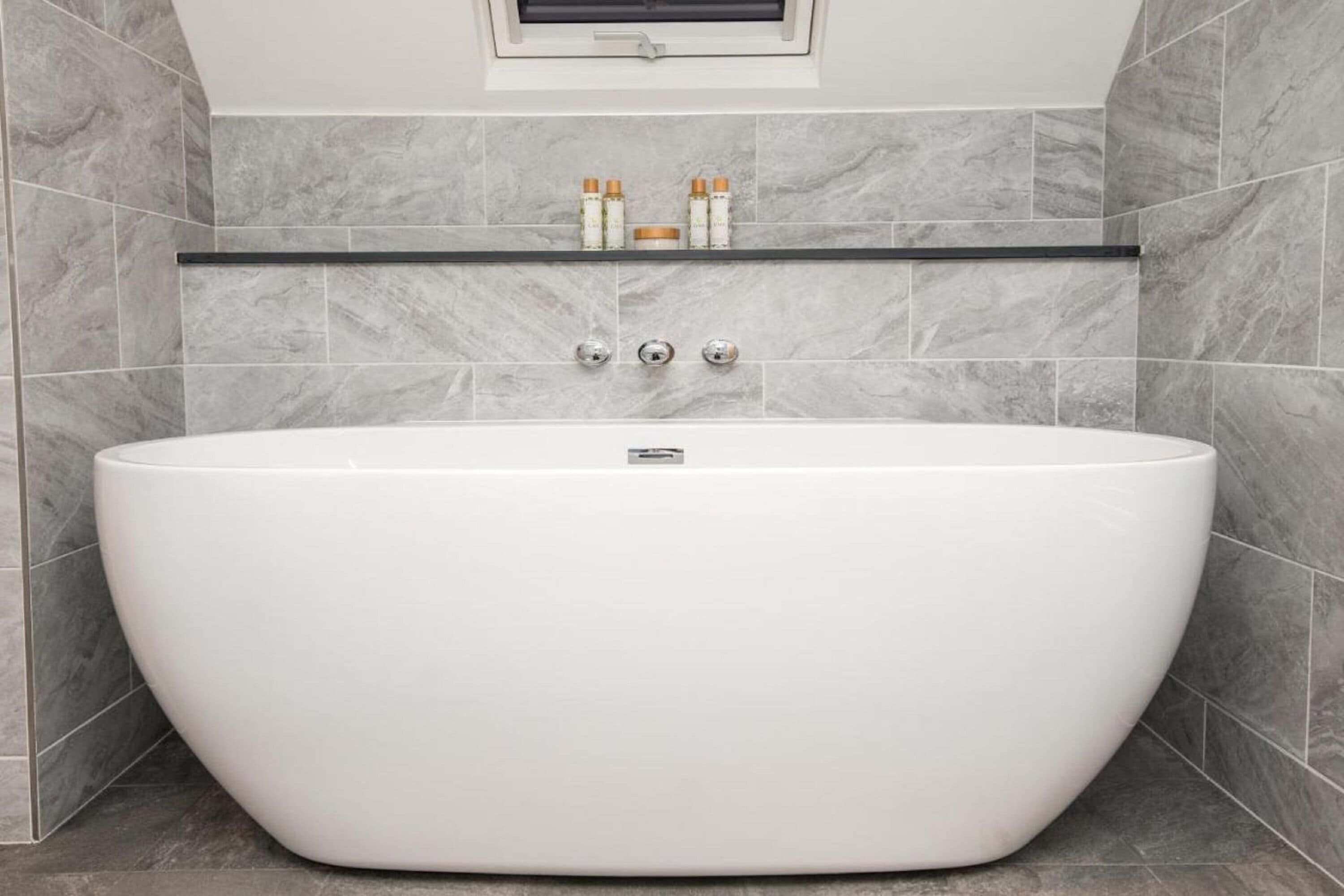 Un baño moderno con una bañera independiente, baldosas de mármol y un estante con artículos de tocador.