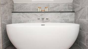 Un baño moderno con una bañera independiente, baldosas de mármol y un estante con artículos de tocador.
