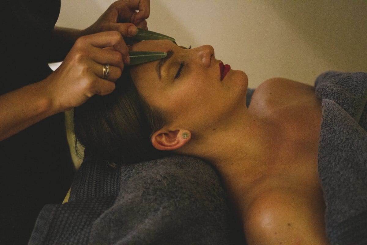 A person lying down with a towel covering their upper body, and another person performing a procedure on their ear.
