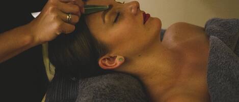 A person lying down with a towel covering their upper body, and another person performing a procedure on their ear.