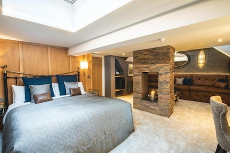 A bedroom with a large bed, a stone fireplace, a sofa, and a TV.