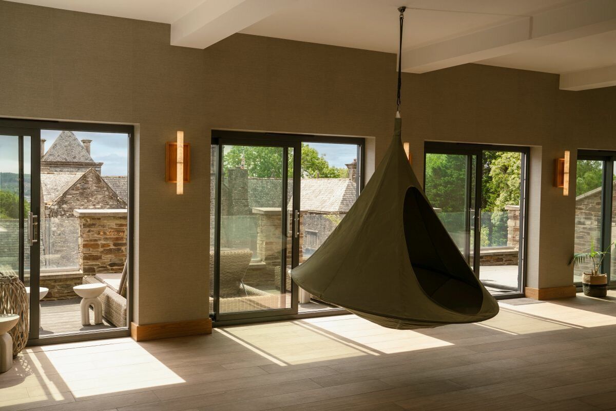 A spacious room with large sliding glass doors leading to an outdoor area, a hanging chair, and a stone wall.