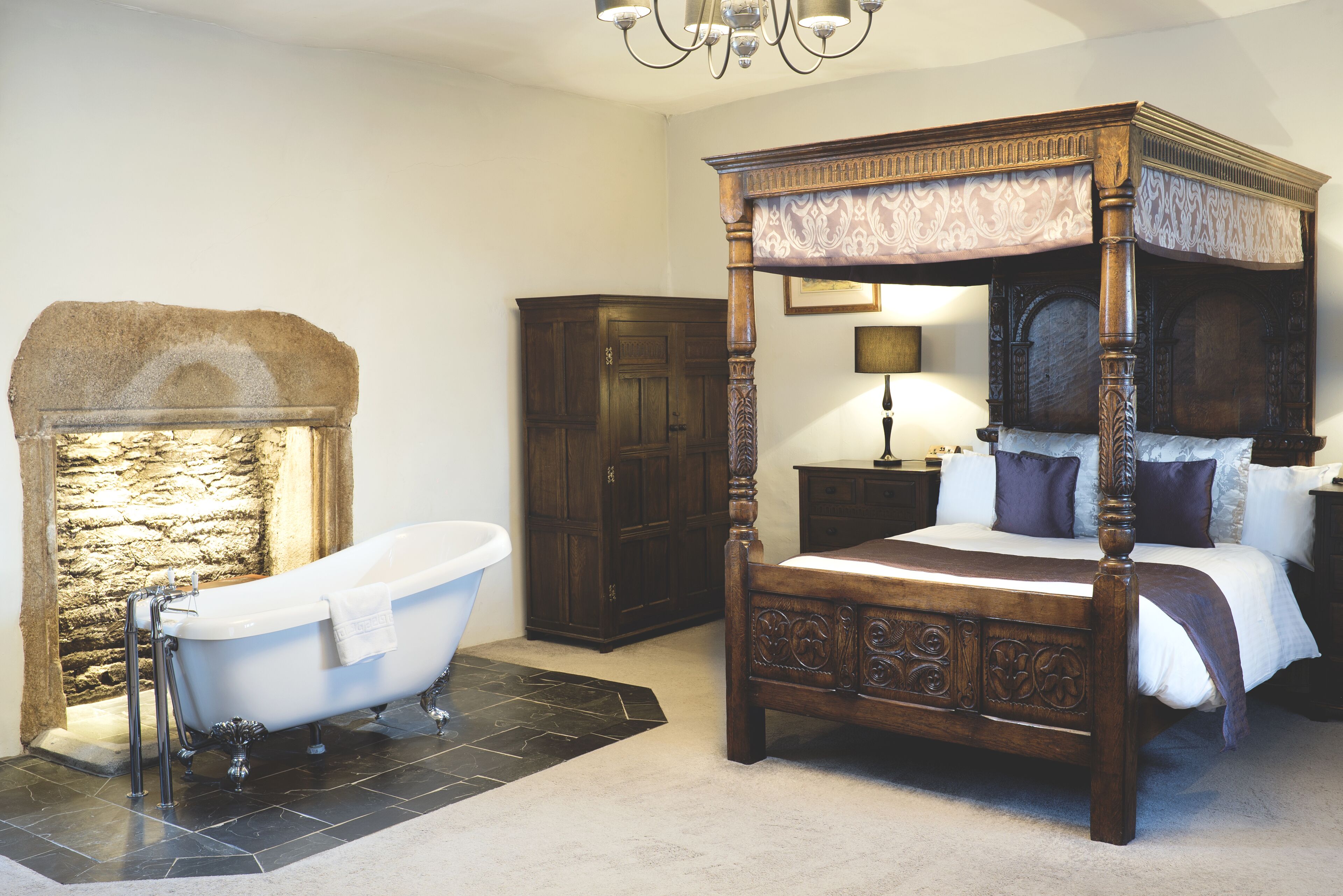 Une chambre à coucher de style traditionnel, avec un lit à baldaquin, une baignoire sur pieds et une cheminée en pierre.