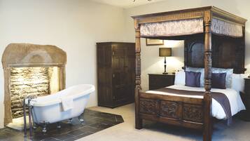 Une chambre à coucher de style traditionnel, avec un lit à baldaquin, une baignoire sur pieds et une cheminée en pierre.