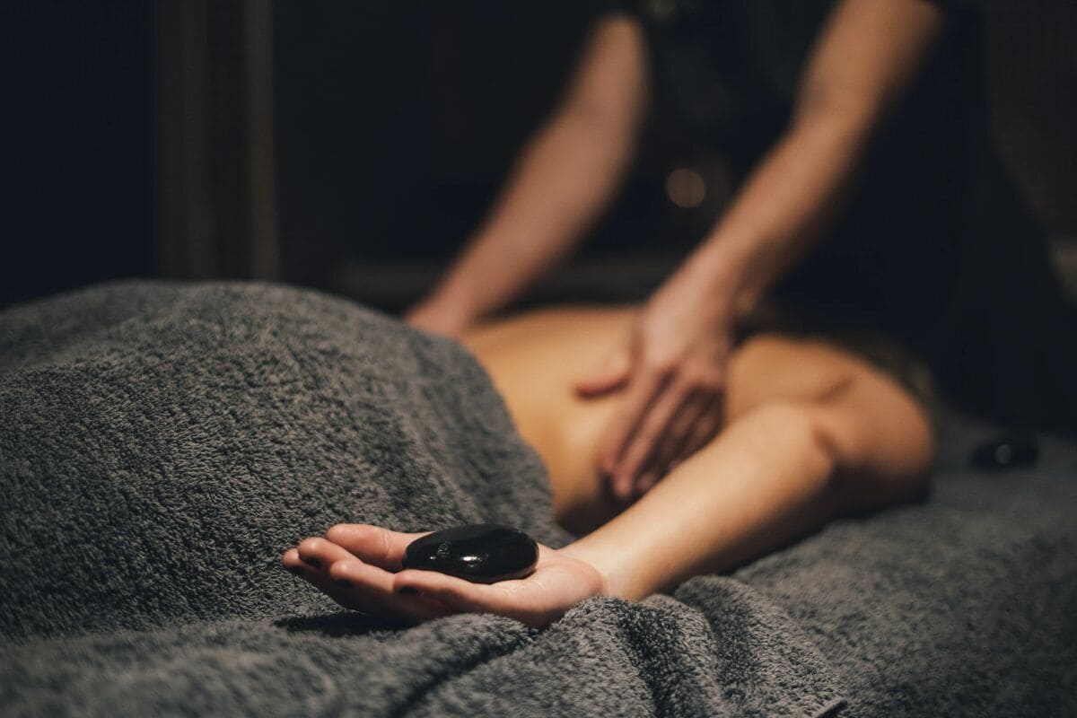 A person lying on a textured surface with a black object in hand, and another person attending to them.