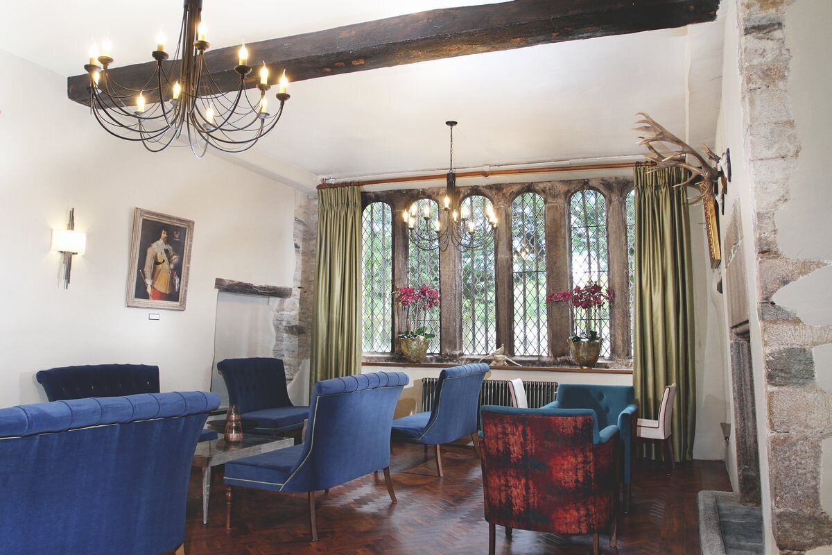 Um quarto com teto de madeira, um candelabro, uma parede de pedra e uma janela com cortinas.