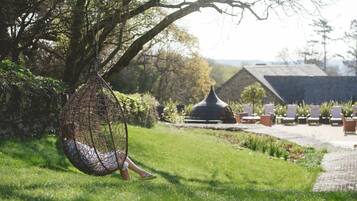 Een hangmat in een weelderige tuin met een prieel en lounge fauteuils op de achtergrond.