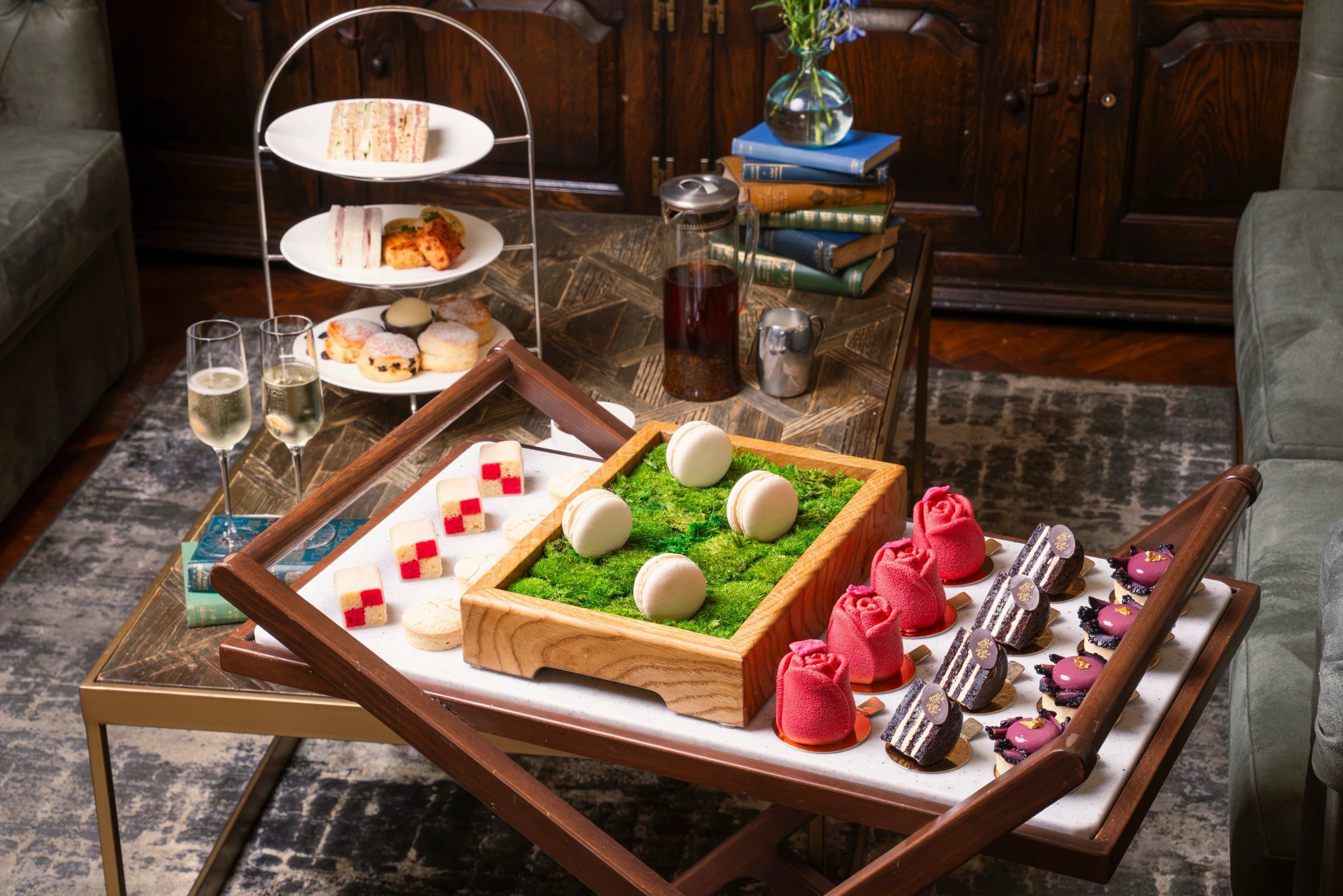 A tray with various pastries and desserts, a glass of wine, and a book stack in the background.