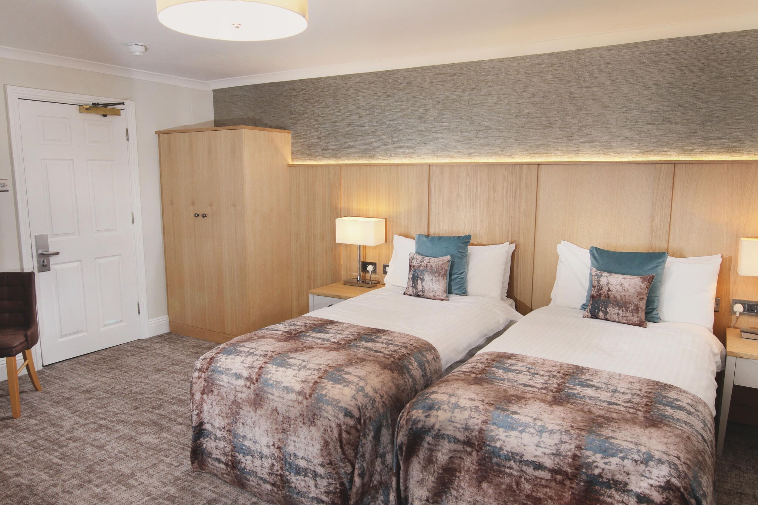 A hotel room with two beds, a wardrobe, a desk, and a chair.