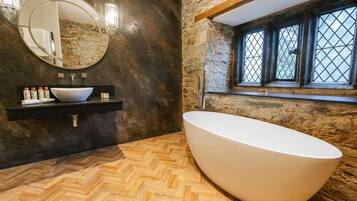 A modern bathroom with a freestanding bathtub, a round mirror, a built-in sink, and a stone wall.