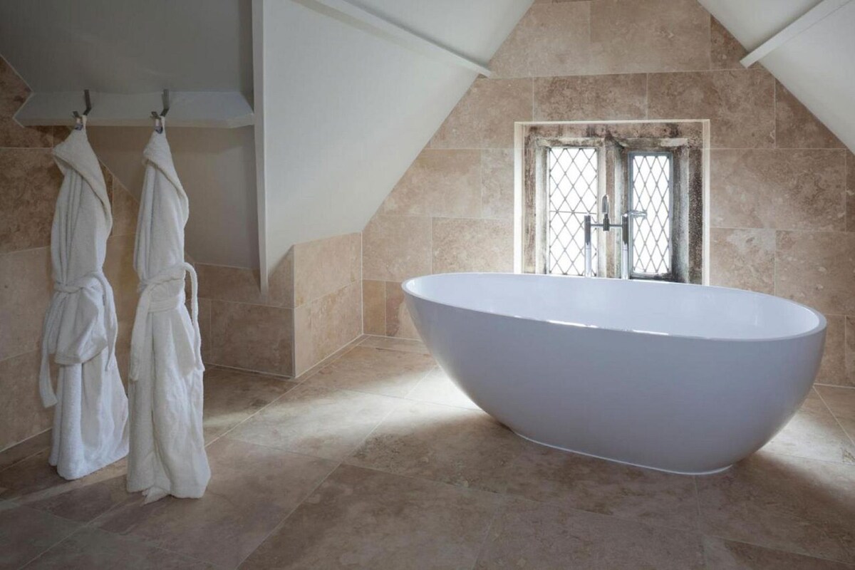 A modern bathroom with a freestanding bathtub, two white towels hanging on hooks, and a window with a metal grille.