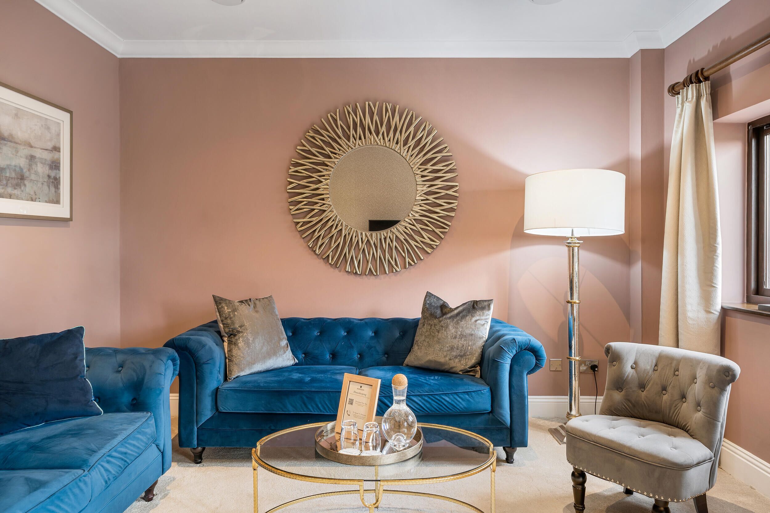 A living room with a blue sofa, a grey armchair, a round coffee table, and a floor lamp.