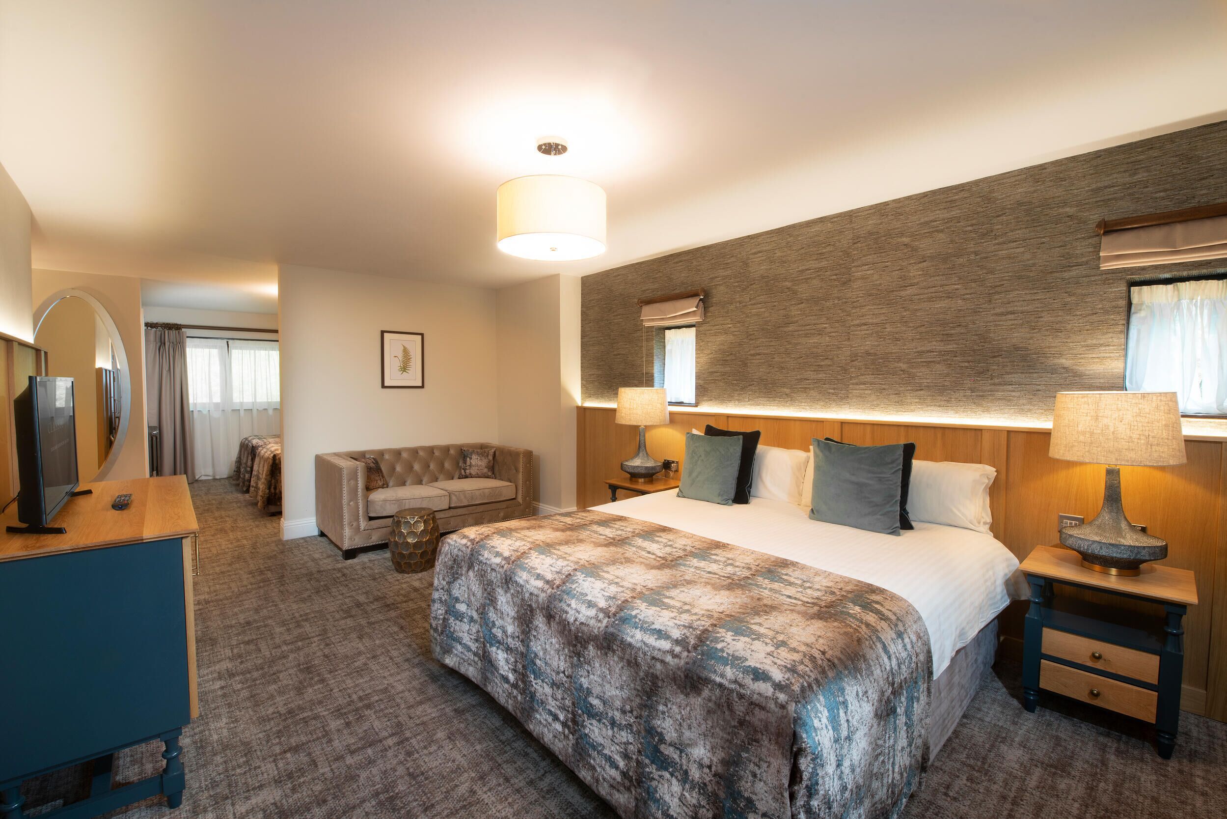 Ein Hotelzimmer mit einem großen Bett, einem Holzkopfteil, einer Sitzecke mit einer Couch, einem Schreibtisch mit Lampe und einem Spiegel.