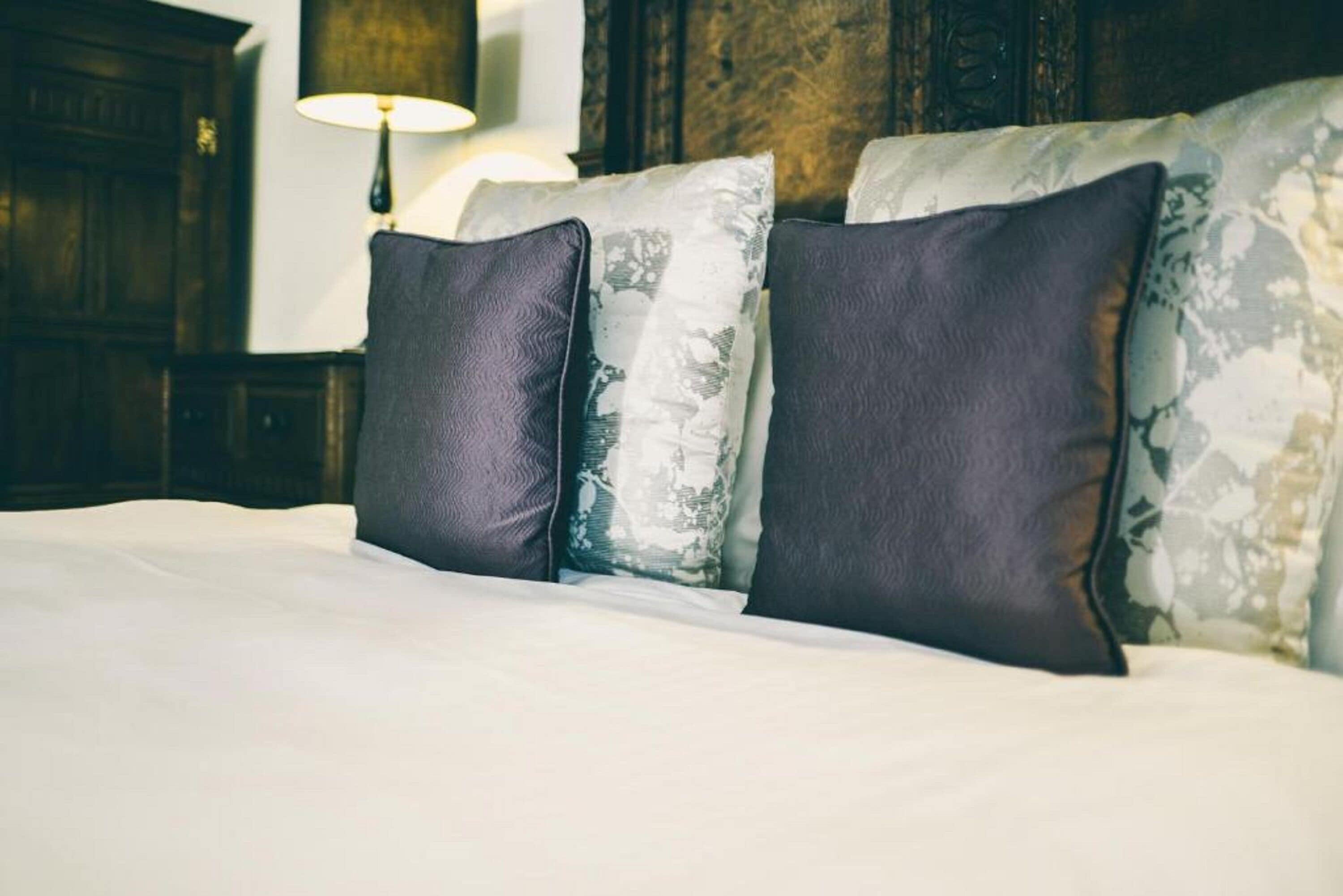 A bed with three pillows, a lamp, and a wooden headboard.