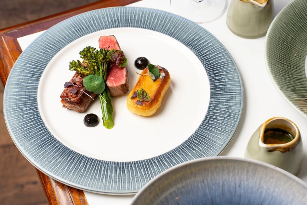 Un plato de comida con diversos elementos, incluyendo carne, verduras y un pequeño pastel, servido sobre un plato blanco con borde azul.