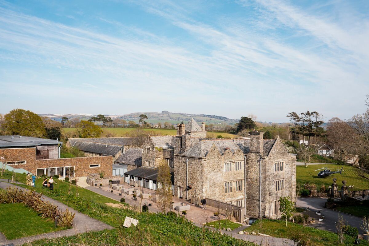 Un bâtiment historique en pierre, doté d’une cour intérieure, entouré de verdure et surplombé d’un ciel dégagé.