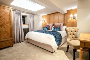 A bedroom with a bed, a wooden wardrobe, a chair, and a table.