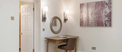 A hallway with a wooden desk, a chair, a round mirror, and two wall-mounted lamps.