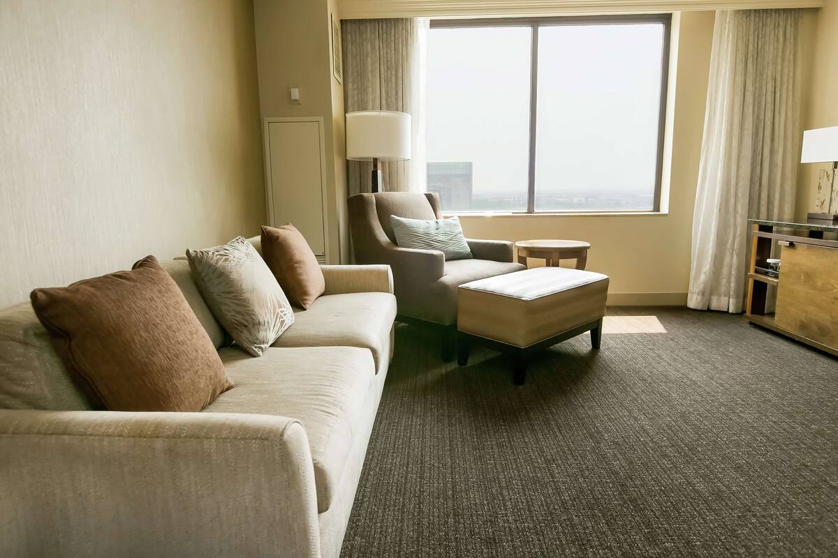 Une chambre d’hôtel avec un canapé, un fauteuil, un pouf et une petite table.