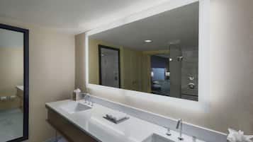 A modern bathroom with two sinks, a large mirror, and a shower area.