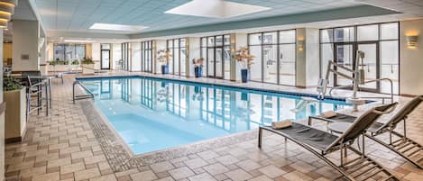An indoor swimming pool with lounge chairs and potted plants.