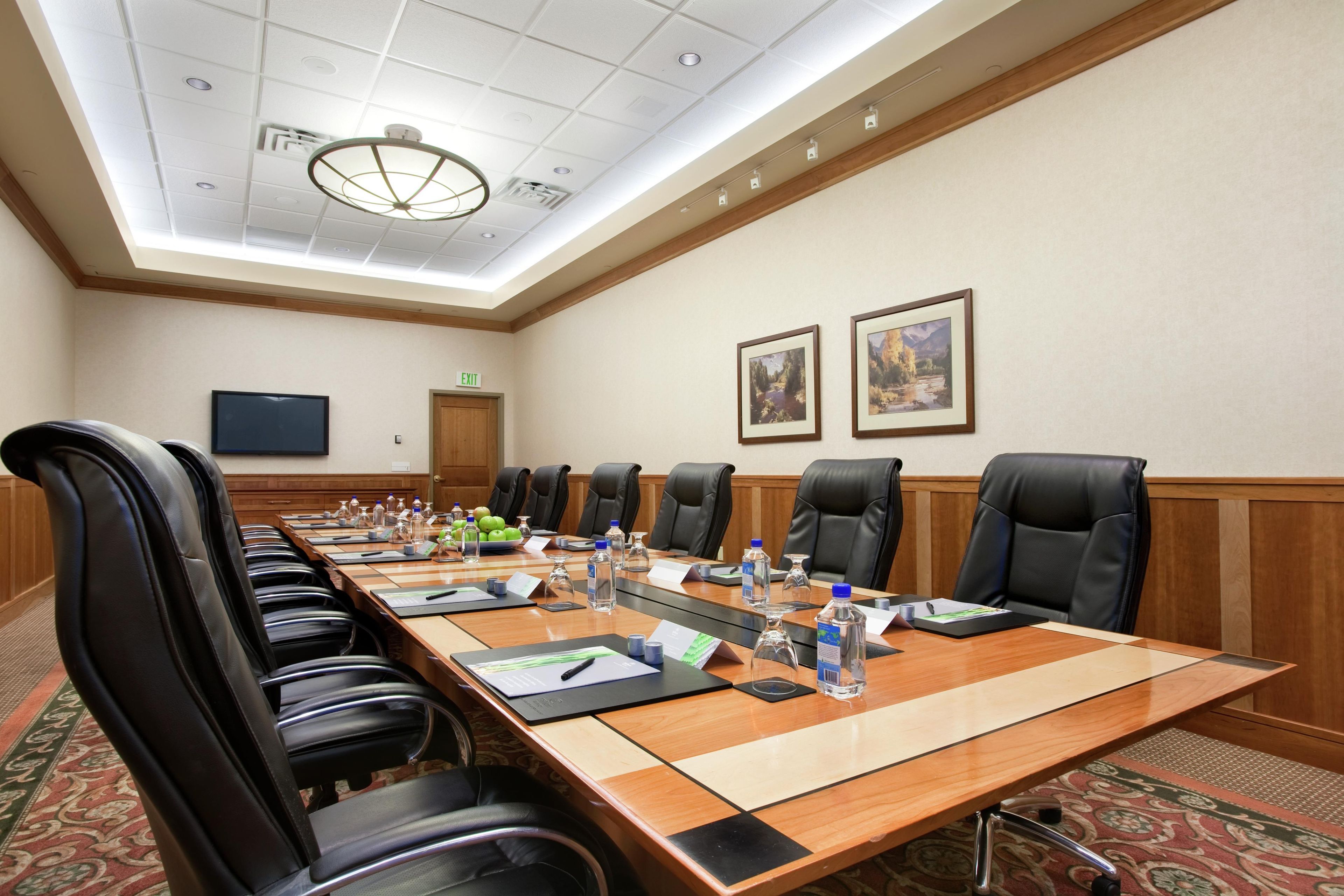 A conference room with a long table, multiple chairs, water bottles, and framed pictures on the wall.