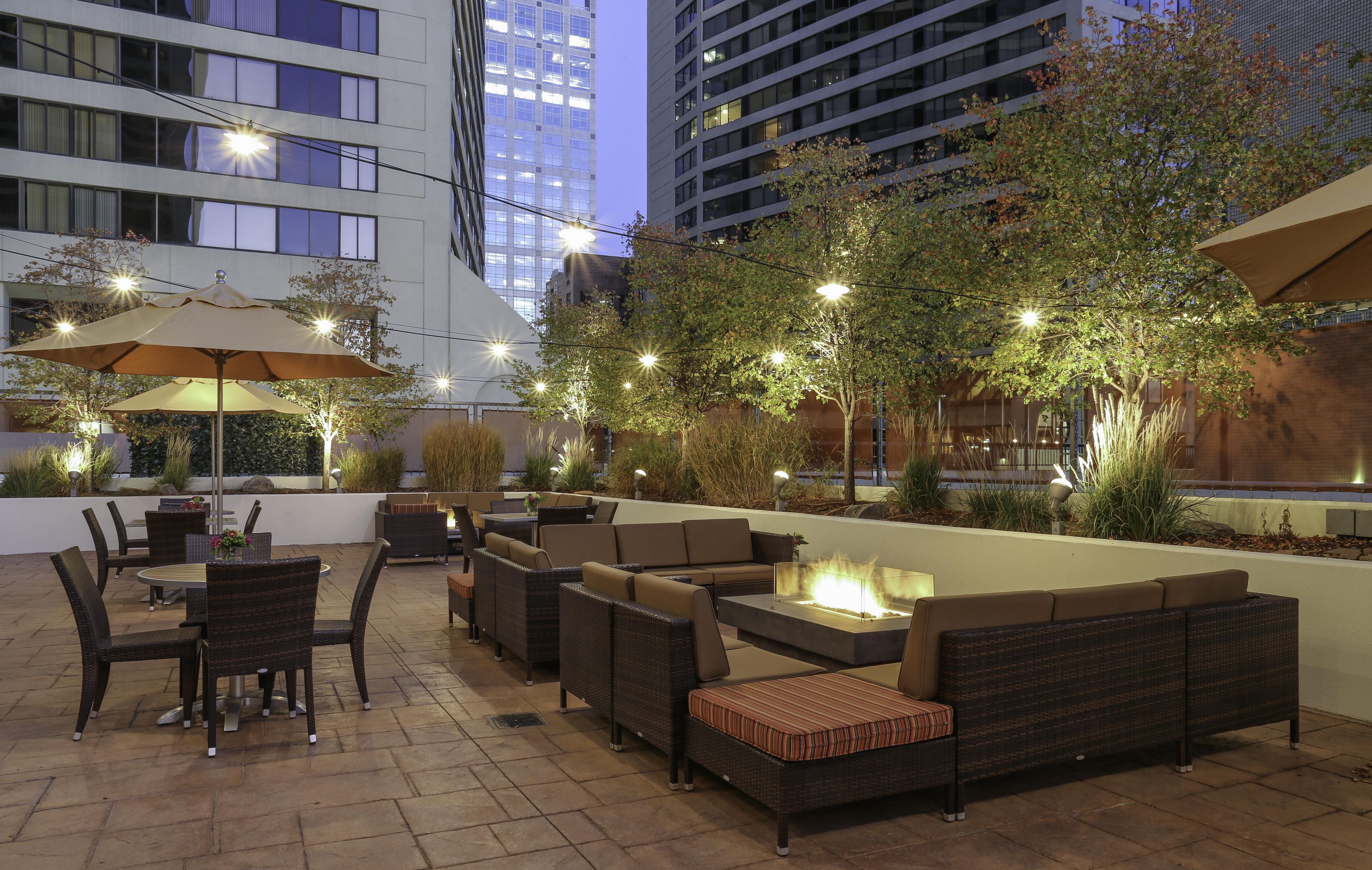 An outdoor patio area with seating arrangements, a fire feature, and ambient lighting.