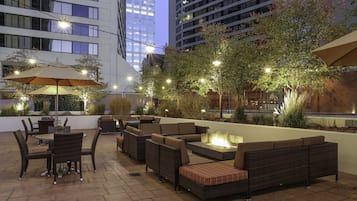 An outdoor patio area with seating arrangements, a fire feature, and ambient lighting.