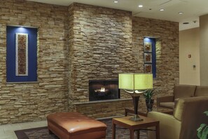 Una pared de piedra con chimenea, asientos de cuero y una mesa con lámpara.