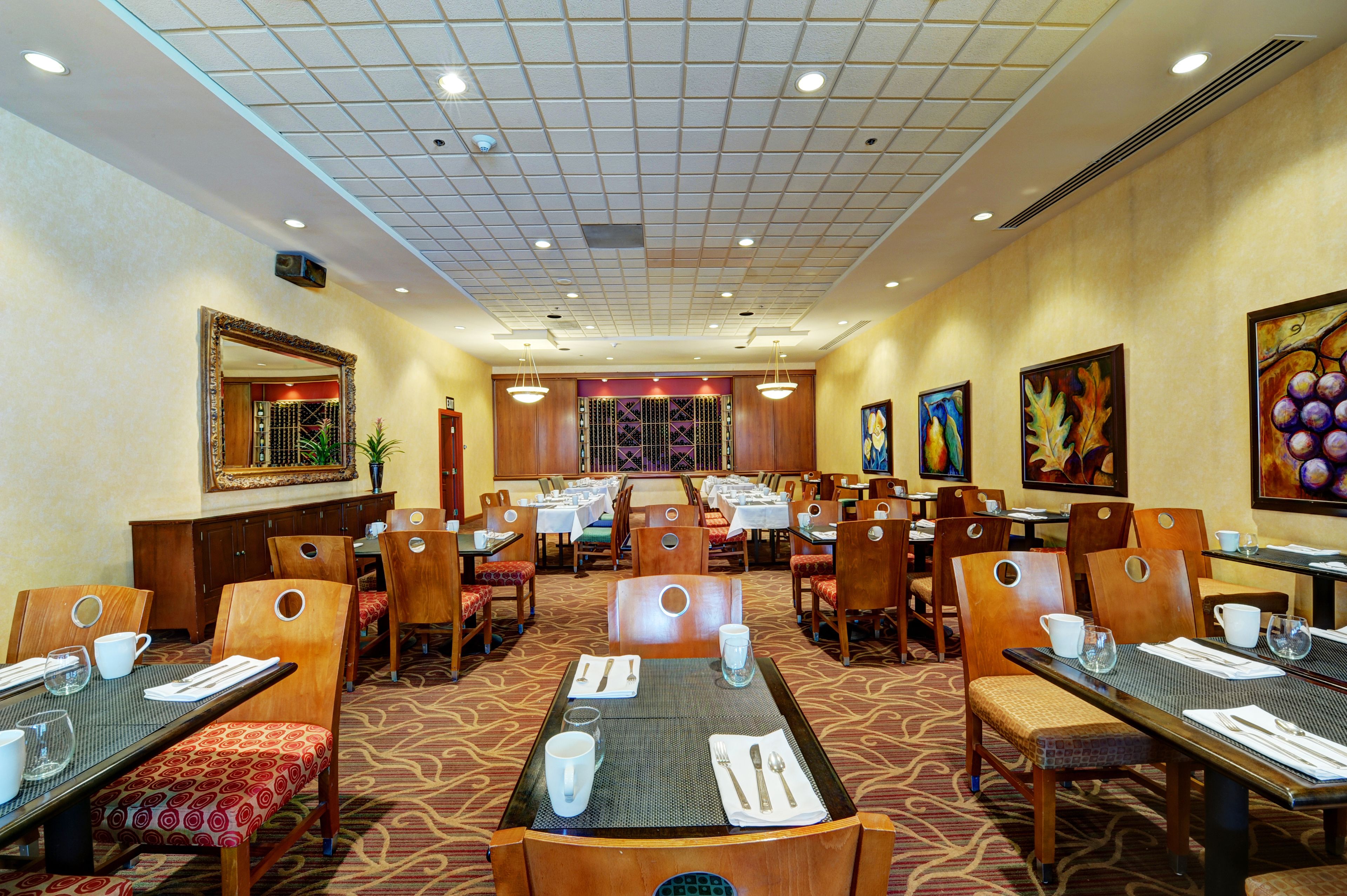 A hotel dining area with multiple tables and chairs, a large mirror, and framed artwork on the walls.