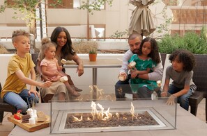 A family around a glass-top table with a fire feature, seated on outdoor furniture.