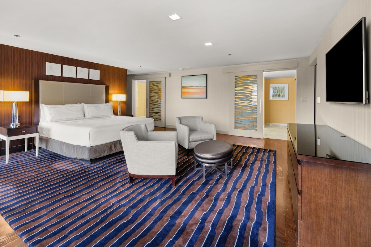 Une chambre d’hôtel avec un grand lit, un bureau, une chaise, une petite table et un téléviseur.