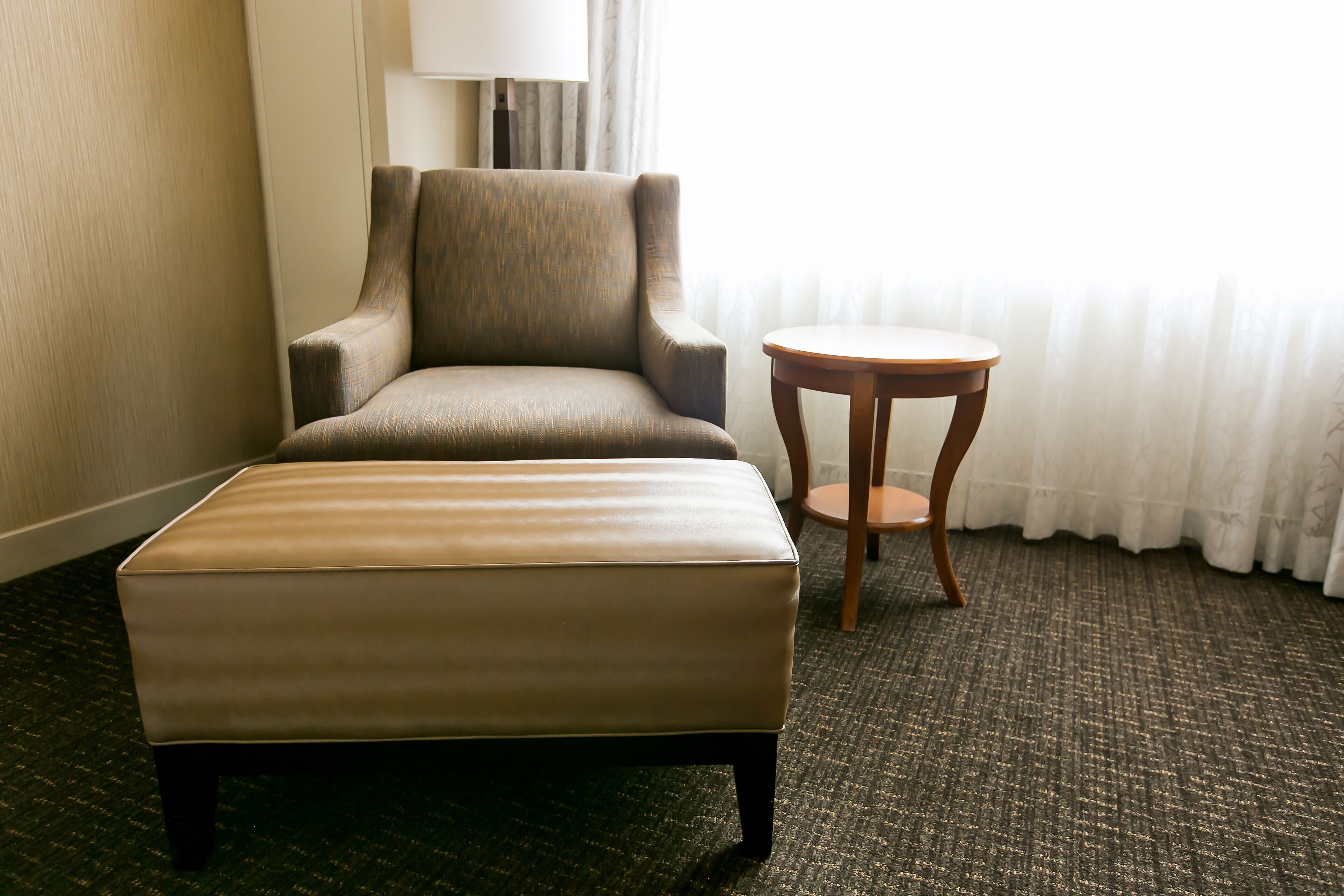 Ein Hotelzimmer mit einer großen, gepolsterten Ottoman, einem Holzstuhl und einem kleinen runden Tisch.