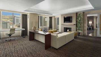 A hotel room with a large bed, a desk, a chair, a TV, a fireplace, and a view of the city.