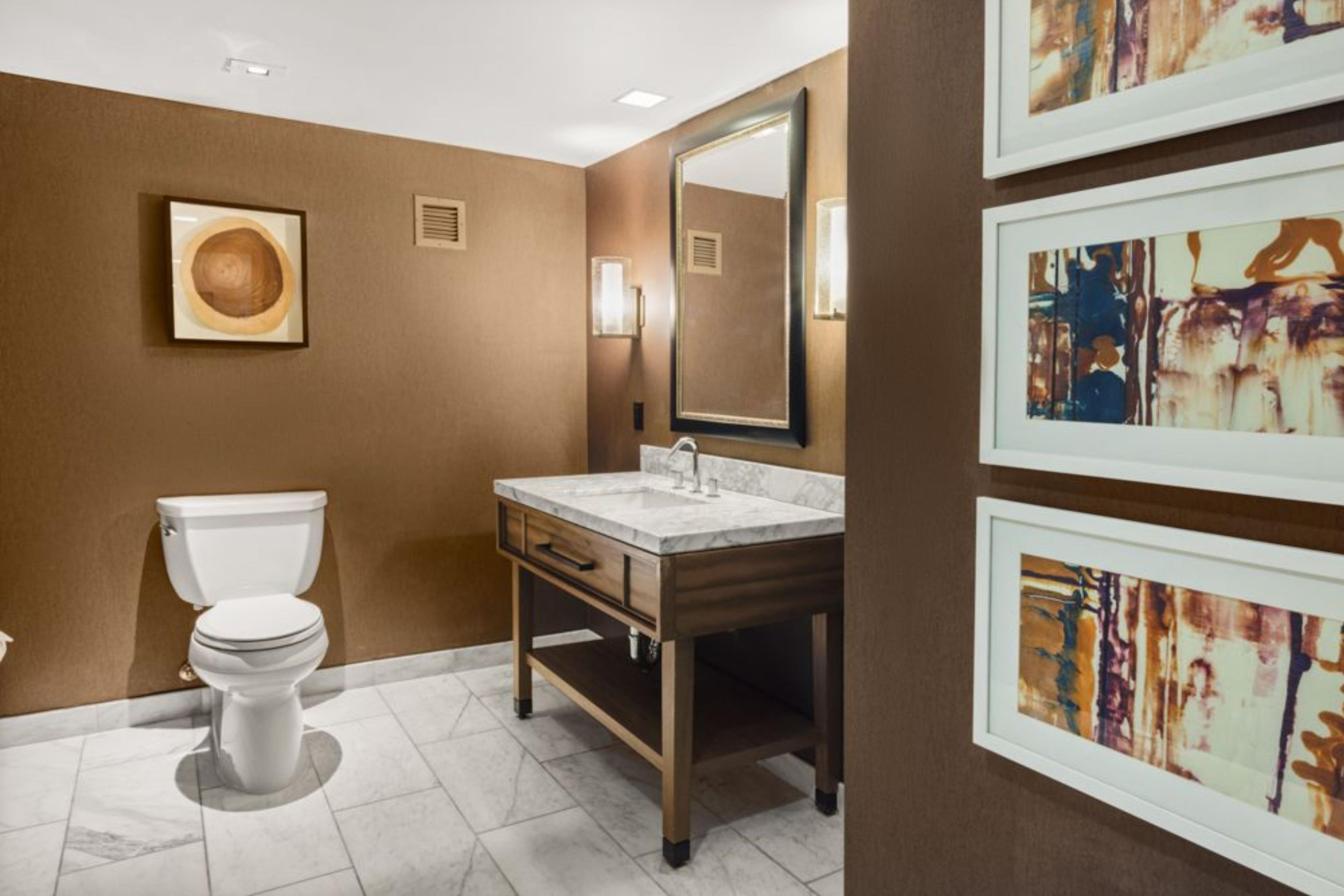 Een badkamer met toilet, wastafel en spiegel. Er hangen kunstwerken in lijsten aan de muur.