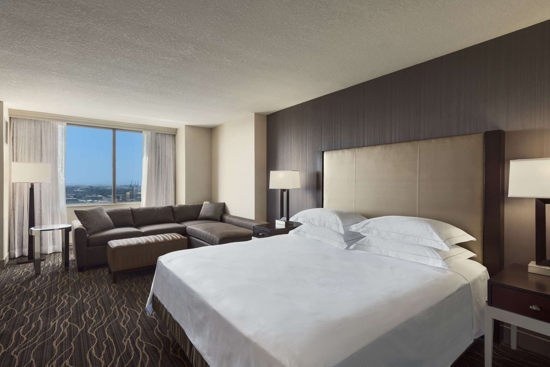Een hotelkamer met een groot bed, een bank, een bureau en uitzicht op de stad.