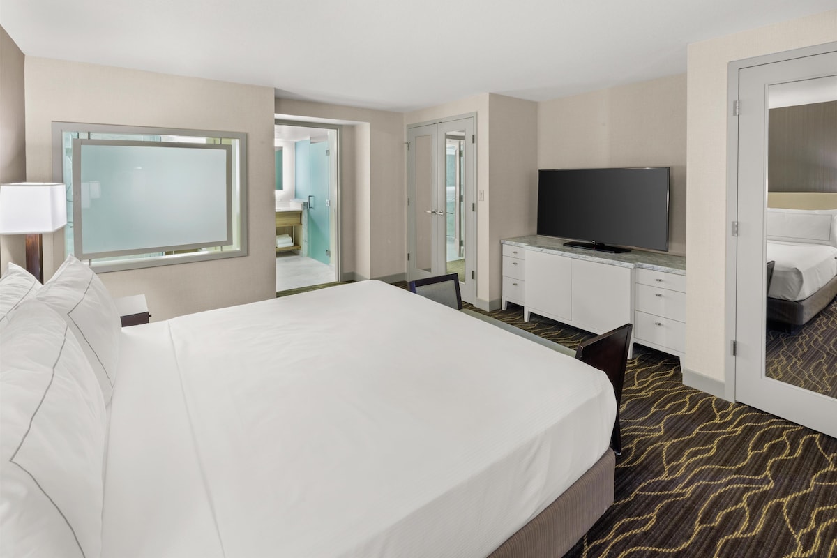 Une chambre d’hôtel avec un grand lit, une télévision, un minibar et une salle de bain visible à travers une porte ouverte.